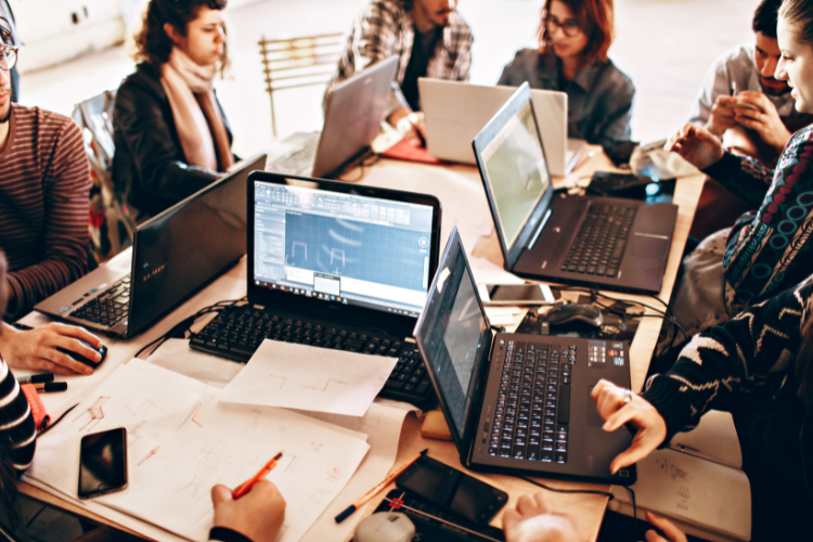 Team collaborating on laptops and documents, working on digital template designs – OneStopCentre