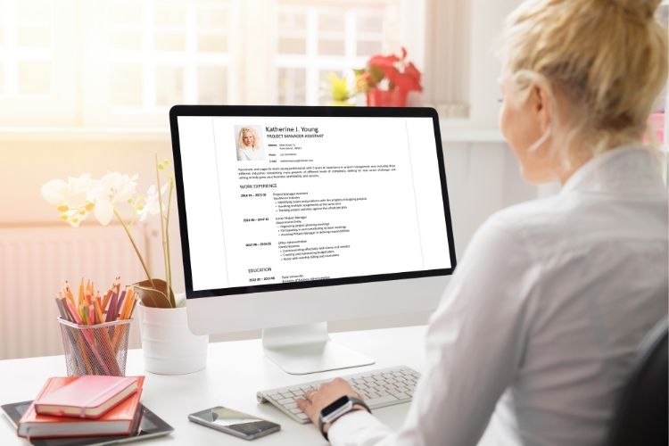 Woman editing professional resume template on desktop computer – modern workspace with sunlight and stationery
